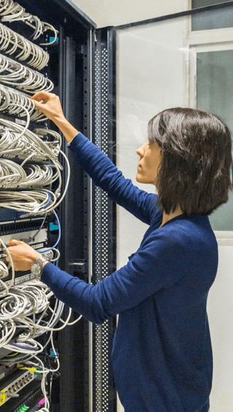 The girl switches fiber-optic Internet wires in a rack with powerful telecommunications.